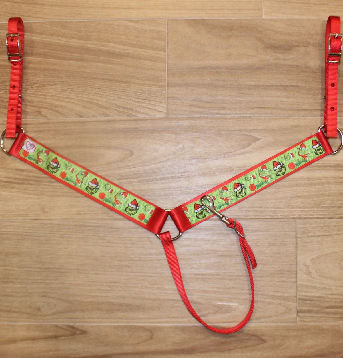 A Christmas-themed horse breast collar featuring red straps, a green patterned center panel and red trim.