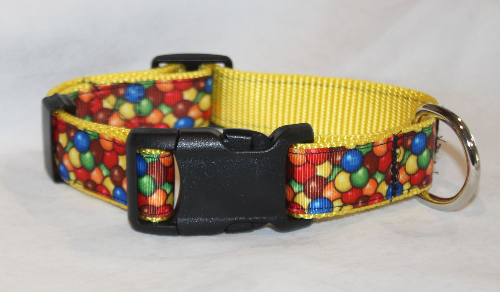 A yellow dog collar with a colorful candy print pattern on the outer strap, featuring a black plastic quick-release buckle and a silver metal ring.
