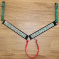 A holiday-themed horse breast collar. The collar features a green and white candy cane cookie pattern, solid green webbing on the side straps, black trim, and a red strap.