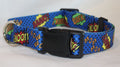 A blue dog collar with a comic book style print featuring pop-art text like 'WOOF!', 'BARK!', 'BOW!', and 'AARF!' in red, yellow, green, and white, with a black plastic buckle and metal ring.