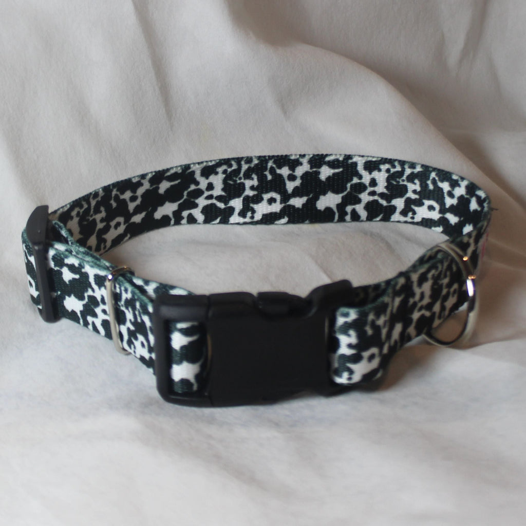 A black and white cow print dog collar with a black plastic quick-release buckle