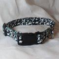 A black and white cow print dog collar with a black plastic quick-release buckle