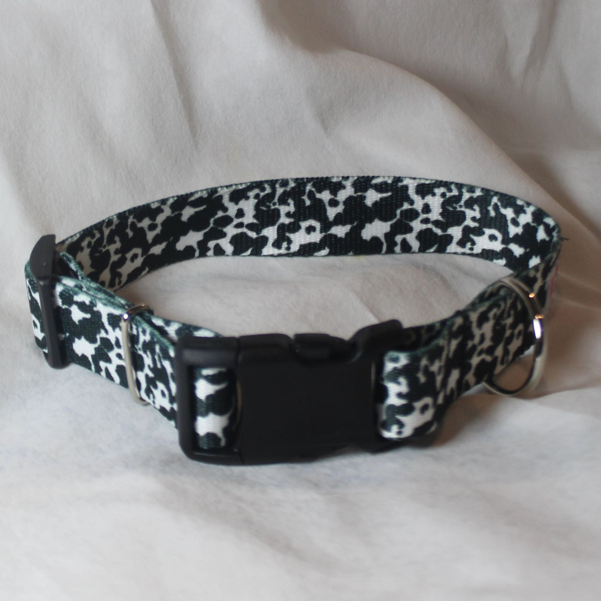 A black and white cow print dog collar with a black plastic quick-release buckle