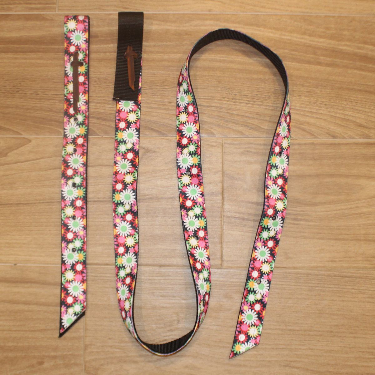A floral-patterned Latigo and Billet Cinch Set. The strap features a dense daisy and poppy pattern in pink, white, yellow, and green, with a solid dark brown leather keeper
