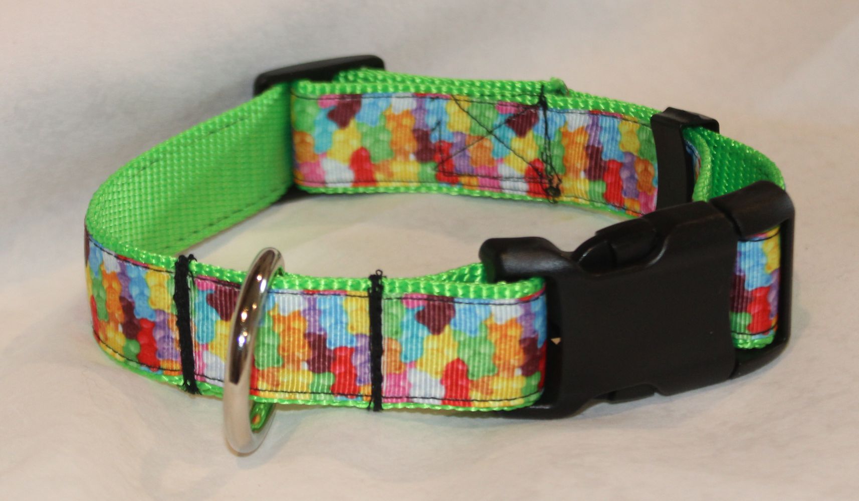 A colorful dog collar with a vibrant gummy bear webbing strap, a solid lime green inner lining, and a black plastic quick-release buckle. It features a silver metal D-ring attachment.