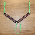 A horse breastcollar laid flat on a light brown wood floor, featuring bright neon green straps and a black central panel with a colorful pumpkin pattern.