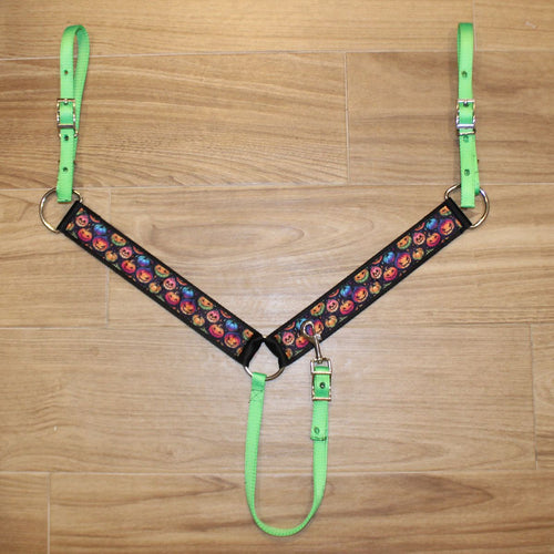 A horse breastcollar laid flat on a light brown wood floor, featuring bright neon green straps and a black central panel with a colorful pumpkin pattern.