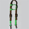 A horse one eared headstall featuring a black fabric body printed with a repeating orange pumpkin pattern, accented with bright green webbing loops and clips