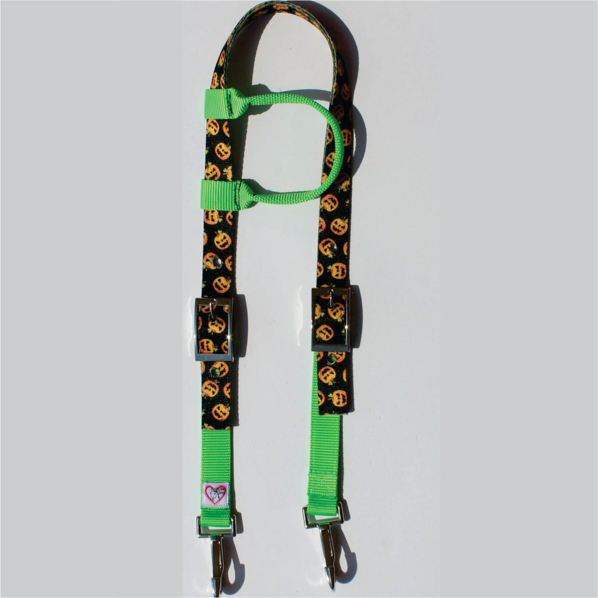 A horse one eared headstall featuring a black fabric body printed with a repeating orange pumpkin pattern, accented with bright green webbing loops and clips