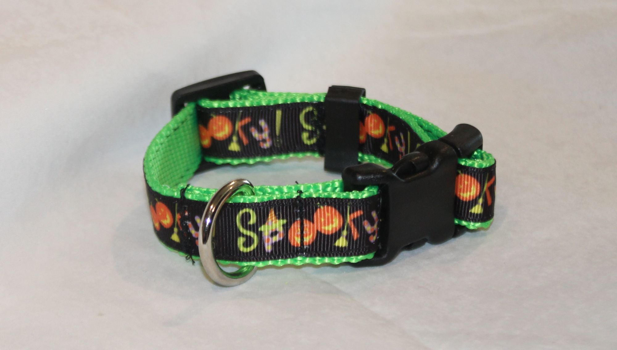 A Halloween dog collar with a bright green inner lining  featuring a 'Spooky' pumpkin pattern, complete with a silver metal ring and black plastic buckle.