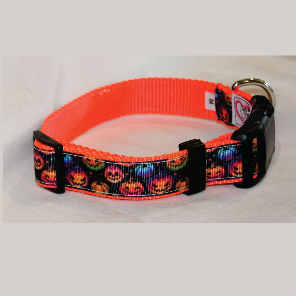 An orange dog collar with a black printed pattern of jack-o'-lanterns and a black plastic buckle