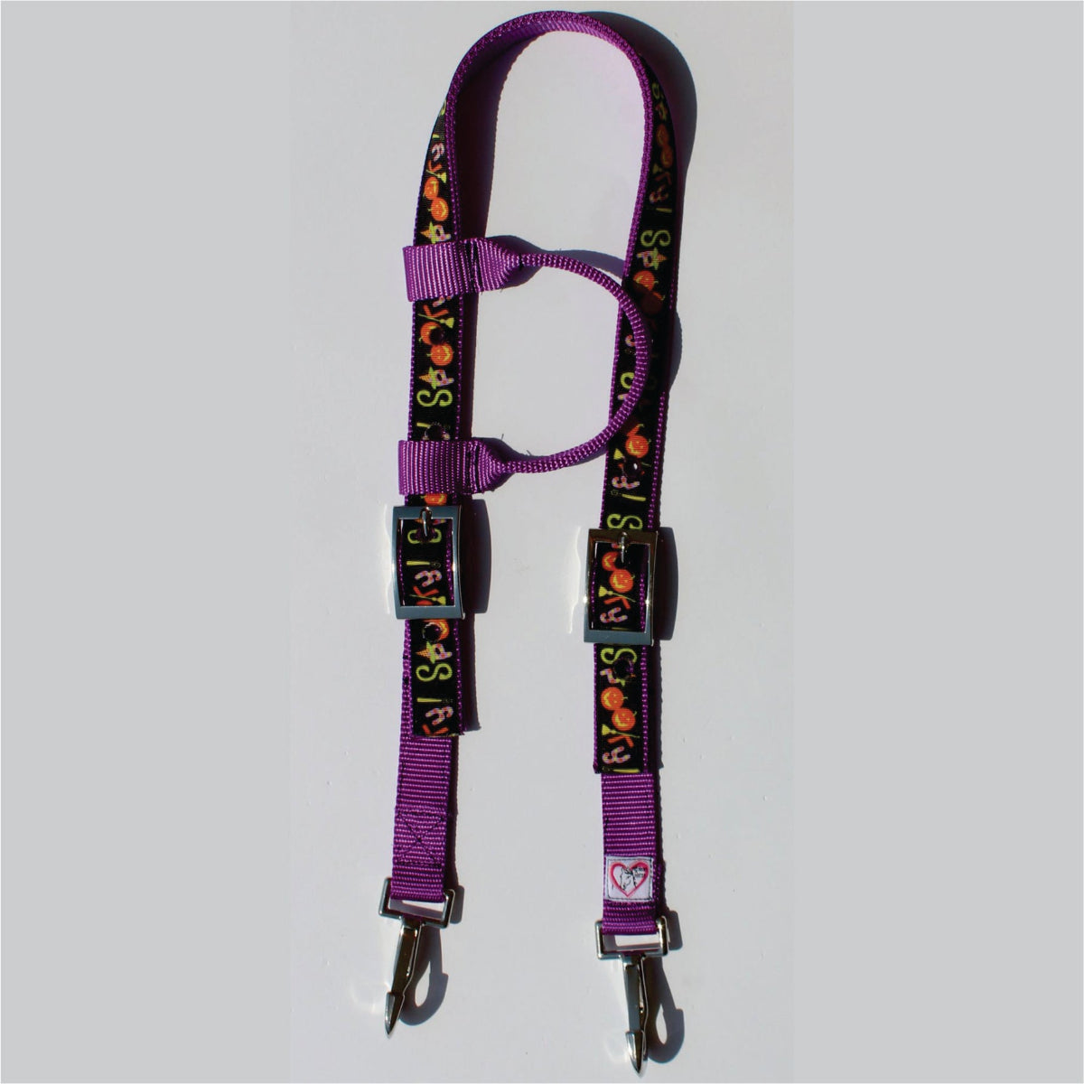 A purple horse headstall with a black patterned webbing featuring orange pumpkins and the word 'spooky' in colorful letters, finished with silver metal clips.
