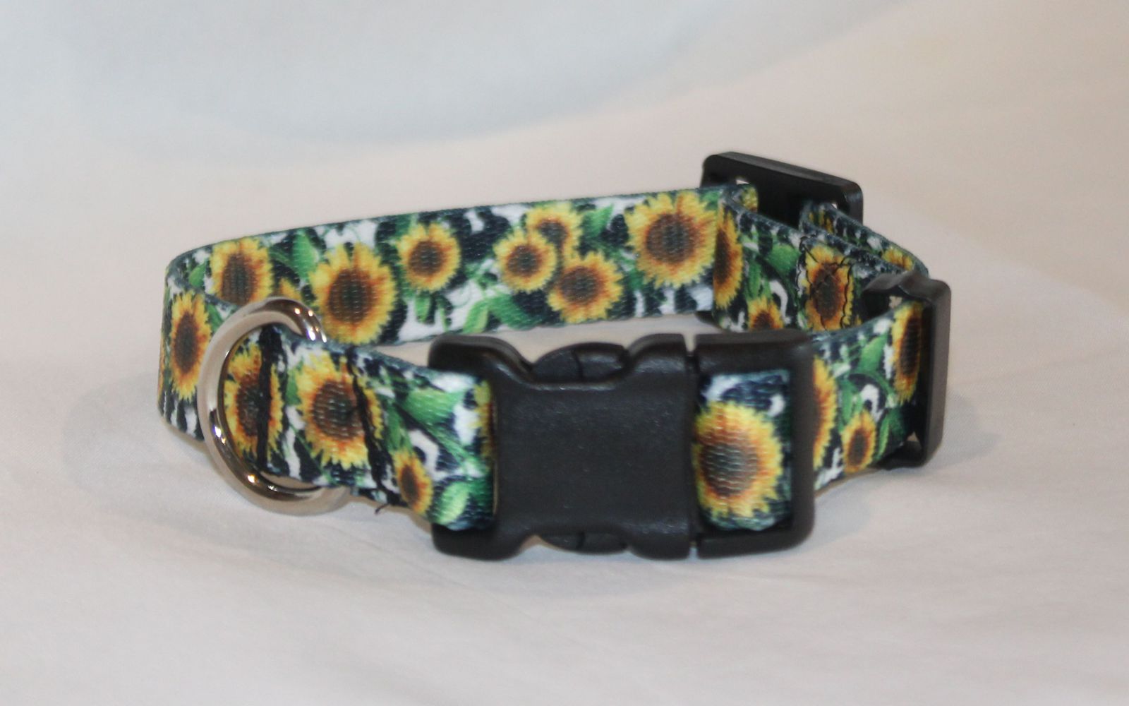 A dog collar with a vibrant sunflower print on a white background, featuring black plastic quick-release buckles and a silver metal ring.