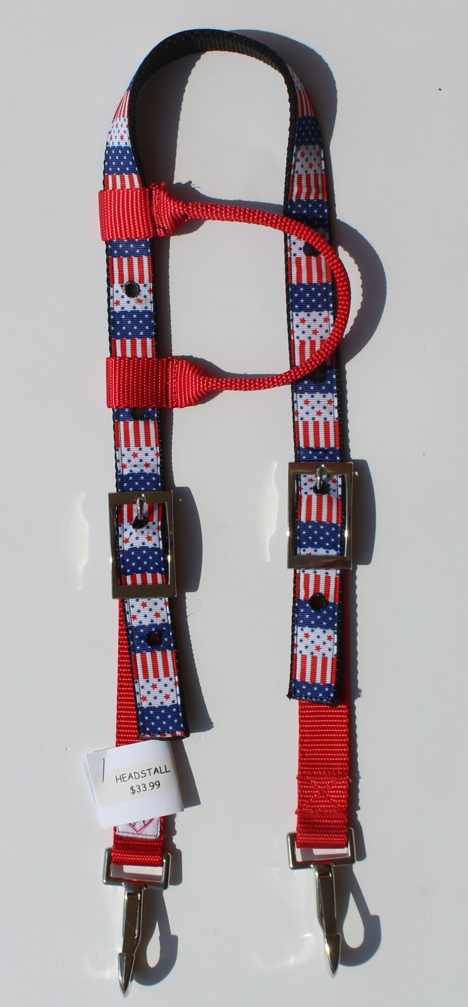 Red, white, and blue American flag patterned horse headstall with metal snap hooks and a white size tag, photographed on a white background.