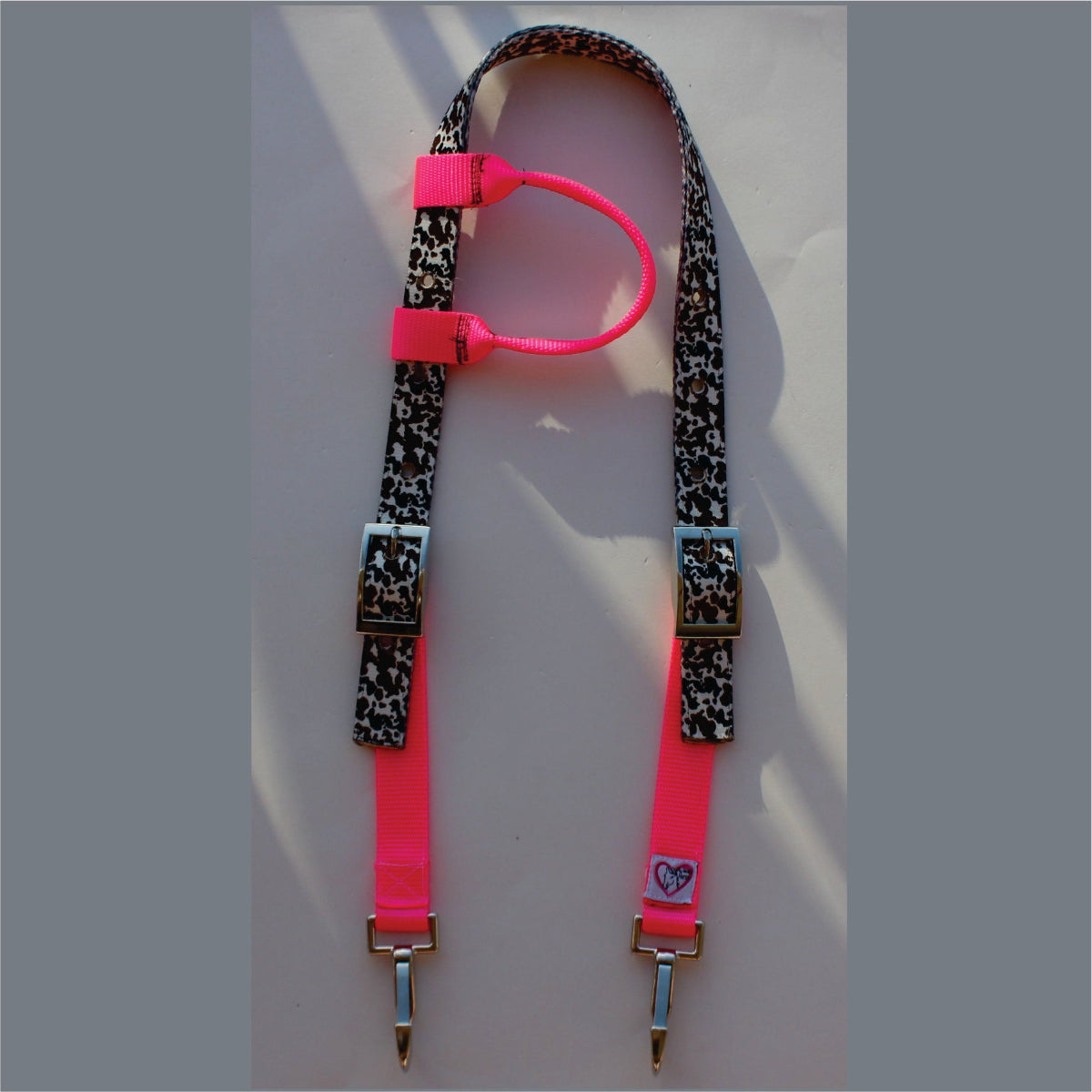 A neon pink and black cow print horse headstall with silver metal clips