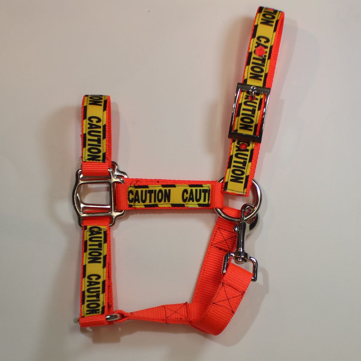 An orange and yellow horse harness with 'CAUTION' tape printed straps and silver metal hardware
